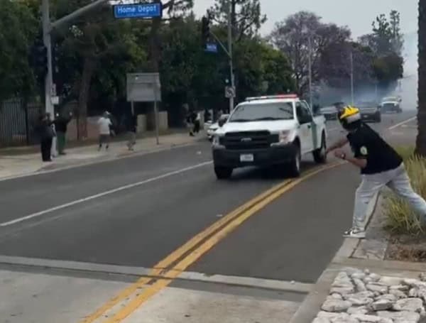 Individual wearing a motorcycle helmet throwing rocks at the windshields of vehicles containing ICE agents.